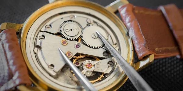 Mecanismo dorado de reloj con pinzas sobre fondo oscuro