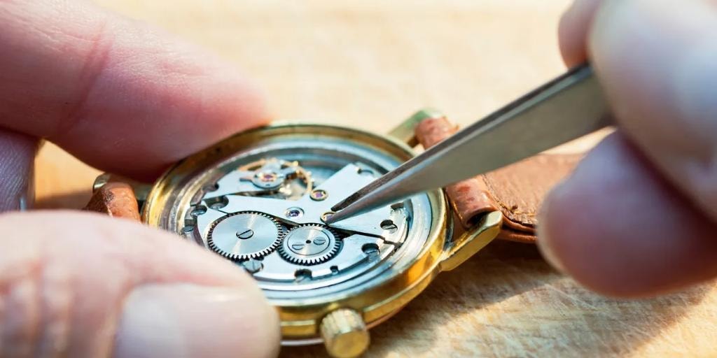 Manos de relojero reparando un reloj dorado con pinzas de precisión
